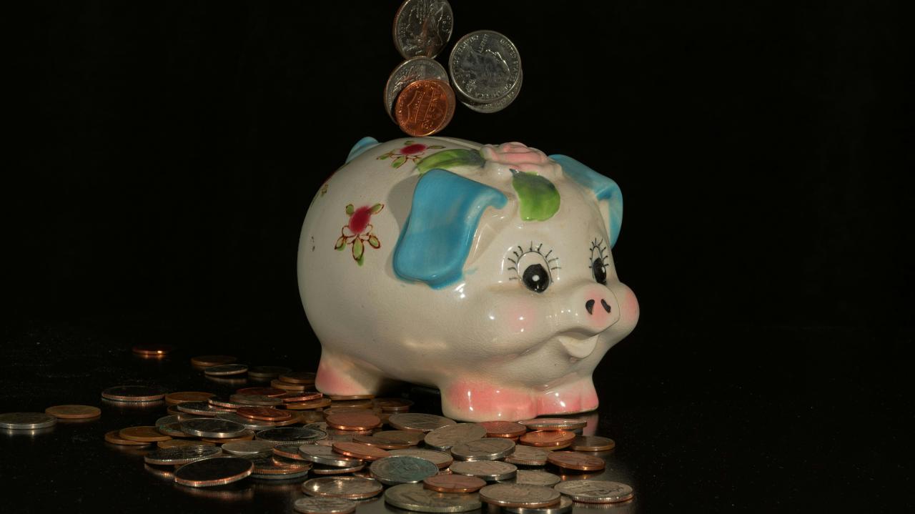 Coins falling into a piggy bank on a black background.