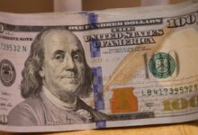 a stack of one hundred dollar bills sitting on top of a wooden table