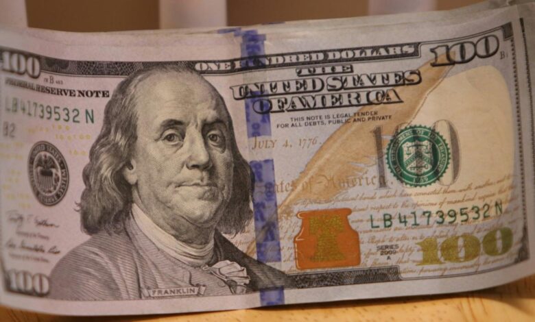 a stack of one hundred dollar bills sitting on top of a wooden table